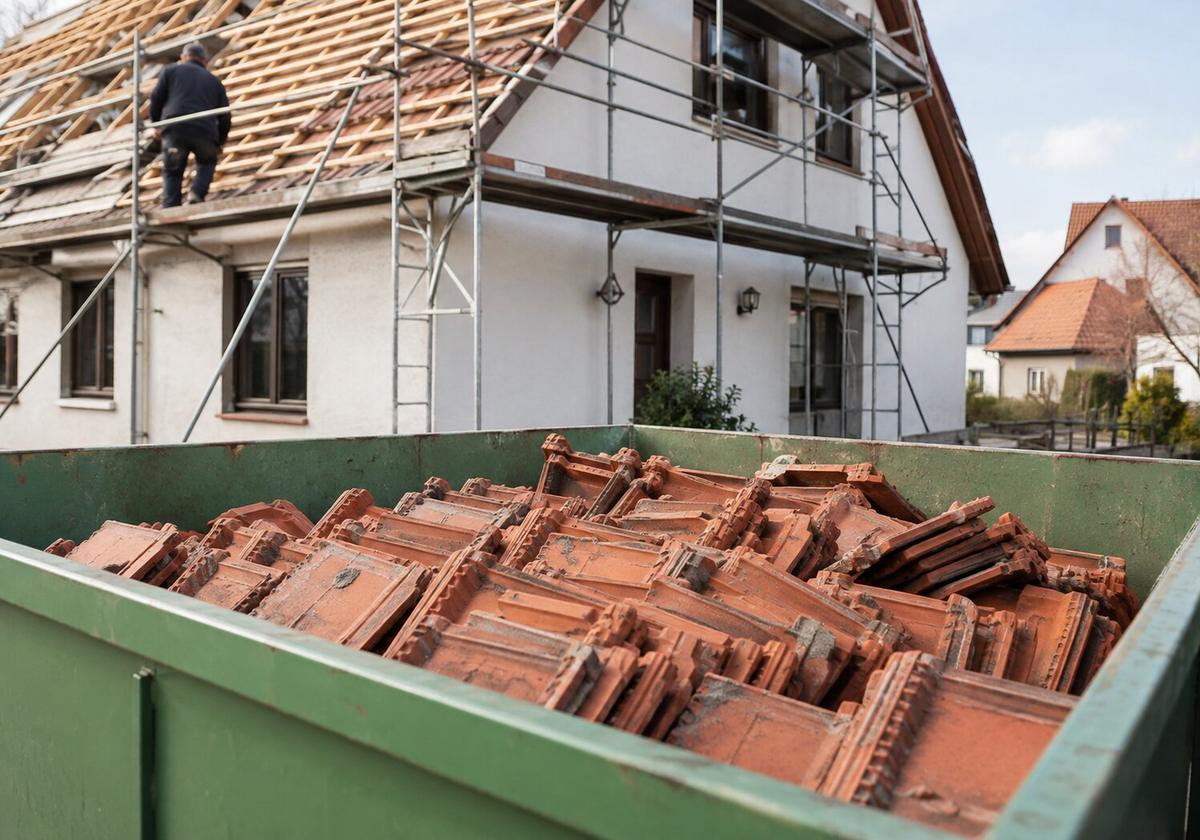 Alte Dachziegel in einem Container vor einem eingerüsteten Haus
