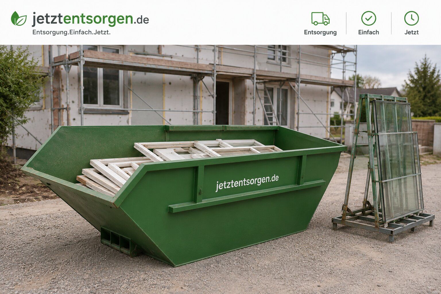 Fenster- und Türen-Container: grüner Absetzcontainer auf einer Baustelle, nur teilweise mit flach geschichteten Fensterrahmen befüllt, daneben Glasscheiben gesichert auf einem Transportgestell